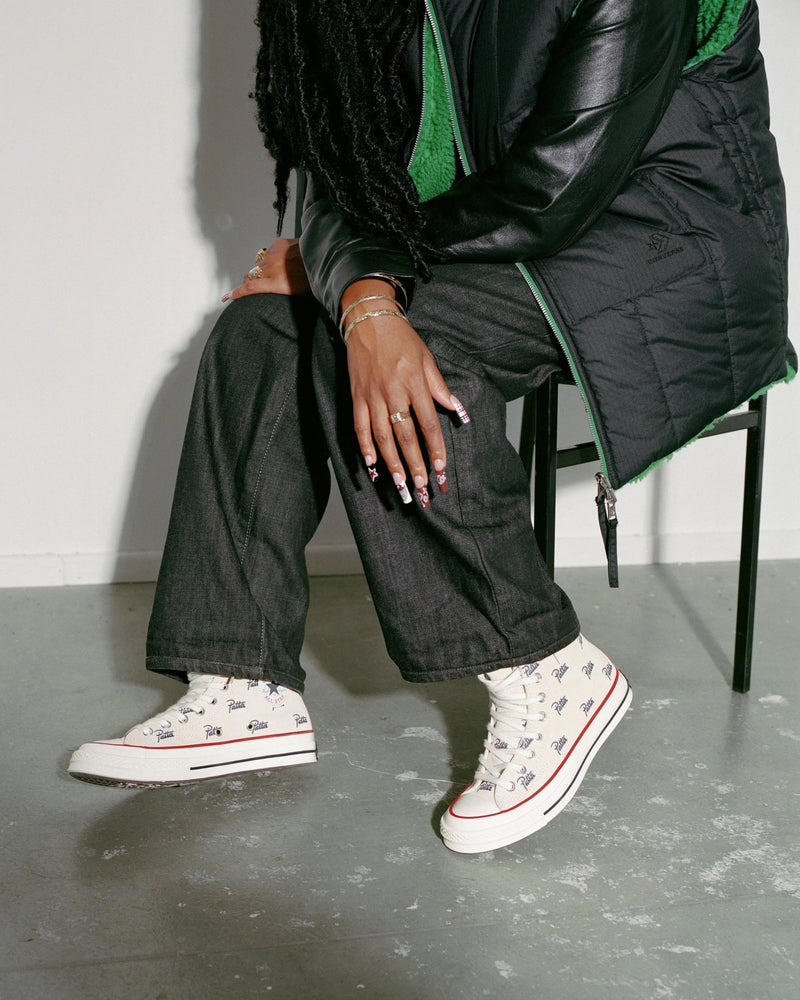 Patta x Converse Chuck 70 Hi sneakers in natural ivory styled on a seated model wearing dark denim.